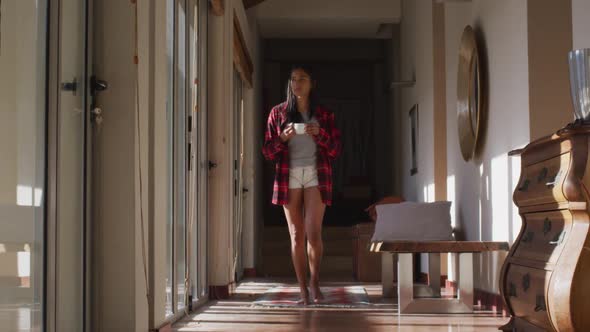 Mixed race woman walking by a window at home alt