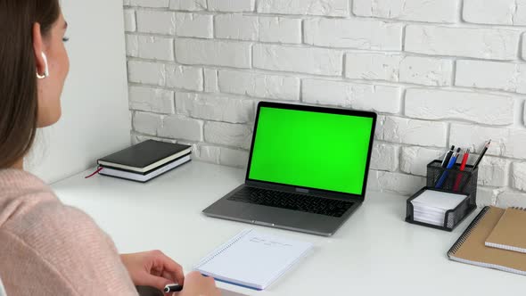 Smiling woman student at home talk listens teacher with green screen laptop alt