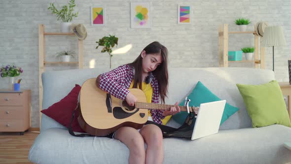 Beautiful Asian Girl with Long Hair in the Living Room of a Modern Home Studying Guitar Watching alt