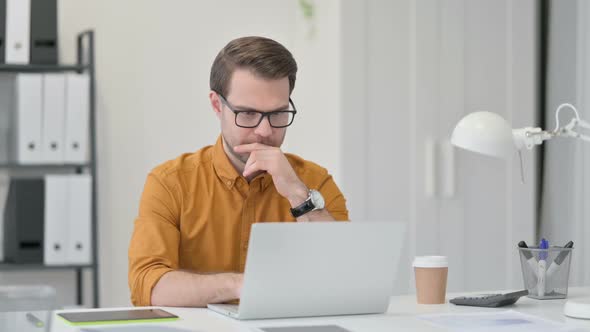 Young Man with Laptop Drinking Coffee in Office alt