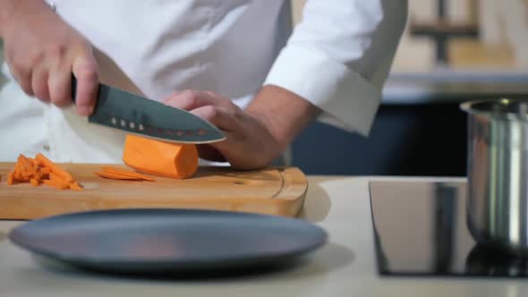 Chef cuts a ripe carrot into slices for a vegetable salad with a knife