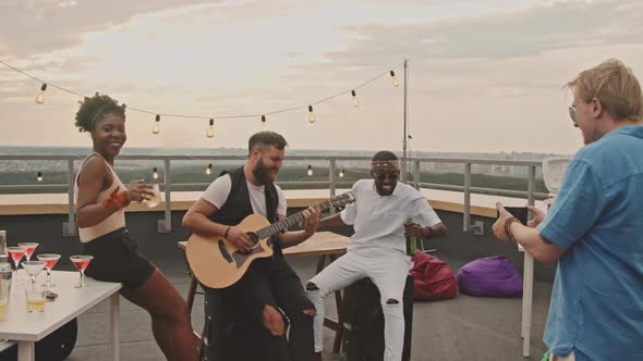 Man Filming Guy Playing Guitar at Rooftop Party alt