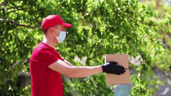 A delivery service worker in red uniform hands over cardboard boxes in medical rubber gloves