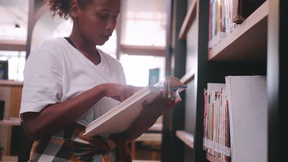 A schoolgirl is searching for books on the library's bookshelf for exam preparation alt