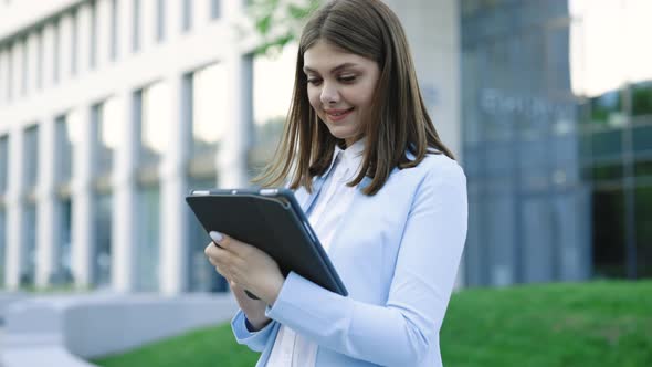 Businesswoman Holding Tablet in Hands Using Business Apps on Tablet Computer Near Office Building