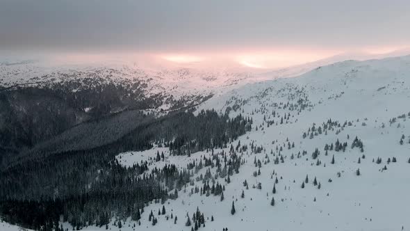 Flying Over Winter Mountain Valley with Clouds Glowing from Sunset