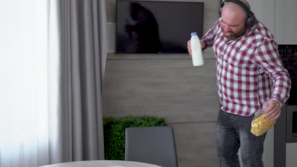 A Bearded Man in Wireless Headphones Walks Through the Kitchen with a Bottle of Milk and Dances alt