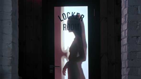 Attractive Woman Silhouette Behind the Locker Room Door Drinking Water From the Bottle alt