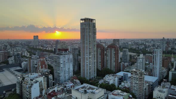 Dolly in flying over Palermo neighborhood buildings and skyscraper at sunset with bright sun hiding alt