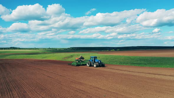 A Tractor Rides on Plowed Field, Sowing Seeds. alt