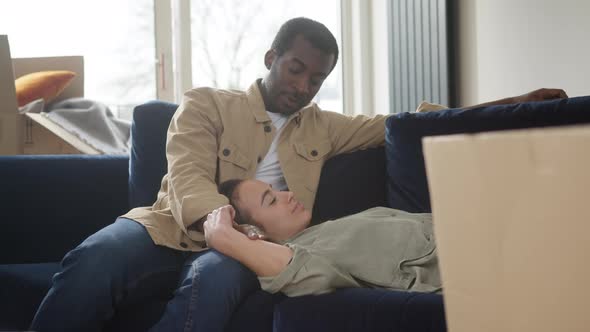 Young Couple In New Home Lying On Sofa In Lounge On Moving Day Surrounded by Removal Boxes