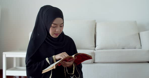 Young Muslim woman wearing traditional clothing and hijab reading Quran