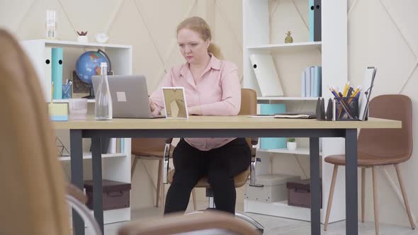 Wide Shot of Serious Woman Working with Laptop in Office and Rubbing Neck. Portrait of Concentrated alt