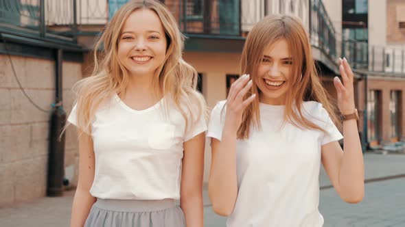 Two young beautiful blond smiling hipster girls in trendy summer clothes alt