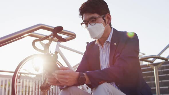 Asian man wearing face mask using digital tablet while sitting on the stairs at corporate park alt