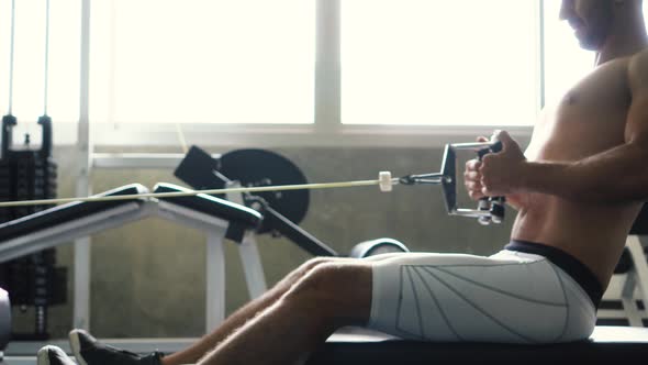 Shirtless Muscular Man Doing Seated Cable Row Exercise on Machine at the Gym alt
