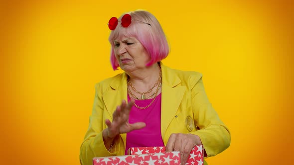 Elderly Granny Woman Opening Gift Box Expressing Disappointment Dislike Gesture to Awful Present alt