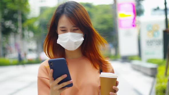 Young asian woman wear medical mask using a smartphone standing in the downtown street