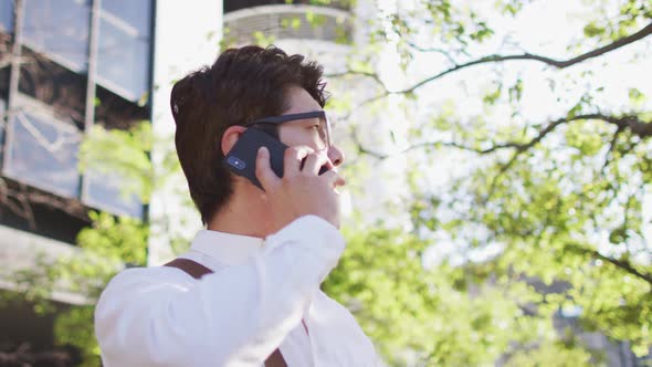 Confused asian man talking on smartphone while standing on the street alt