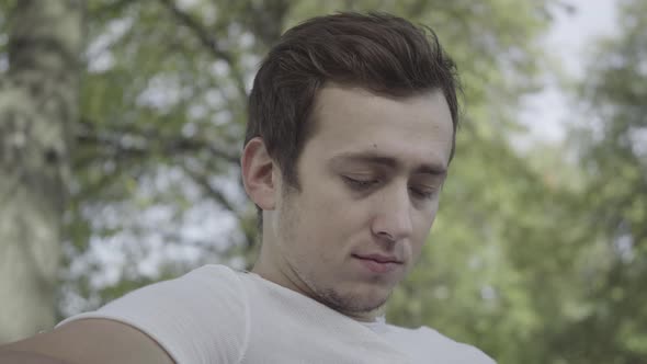 Headshot Portrait of Thoughtful Sad Young Man Sitting in Sunny Summer Park Thinking Looking Away alt