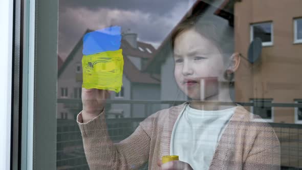 Little Girl Draws the Flag of Ukraine on the Window
