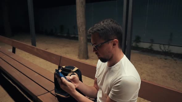 Alone Man Is Sitting Alone in Park in Evening, Looking for a Net for Phone alt