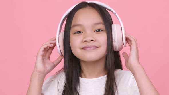 Cute Little Asian Girl in Wireless Headphones Listening to Dynamic Music Dancing and Smiling to alt