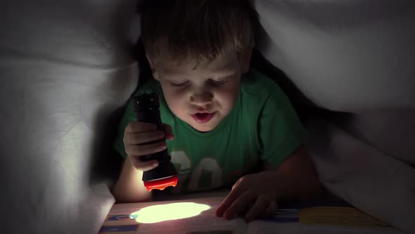 Little Boy Reading a Book at Night Under a Blanket with a Flashlight