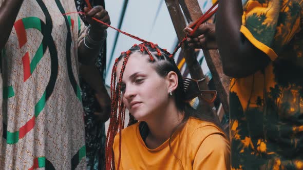 African Woman Weaving African Braids with Red Kanekalon Outdoor Zanzibar Africa alt