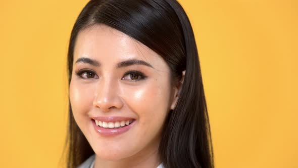 Close up of cheerful attractive Asian woman face smiling in isolated studio yellow background