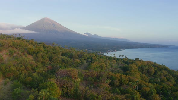 Beautiful Aerial View of Green Tropical Jungle and Ocean Against Distant Volcanos and Mountains alt