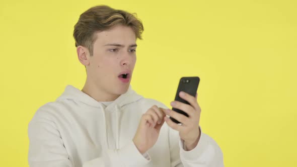 Young Man Loss on Smartphone on Yellow Background alt