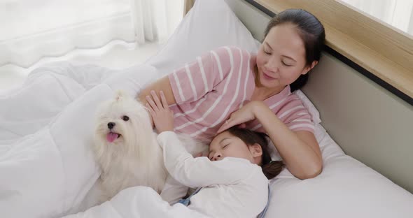 Mother and daughter playing with white dog on bed 2