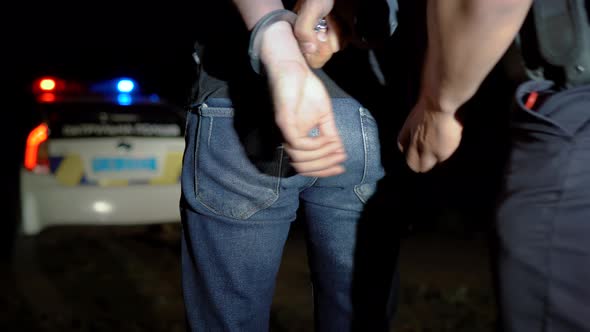 Police Officer Puts Handcuffs on Arrested Man at Night and Leads Him to a Police Car alt