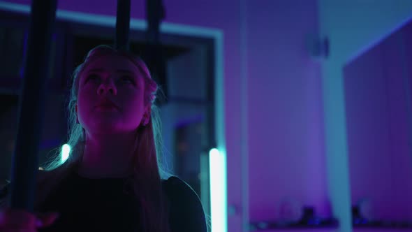 A Woman Does Sports Yoga in the Air on a Hammock in Neon Light Performing Graceful Exercises and alt