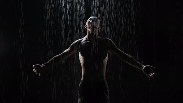 Portrait of Pumped-up Guy Rising Hands at Night in the Rain on Black Background. Close-up of alt