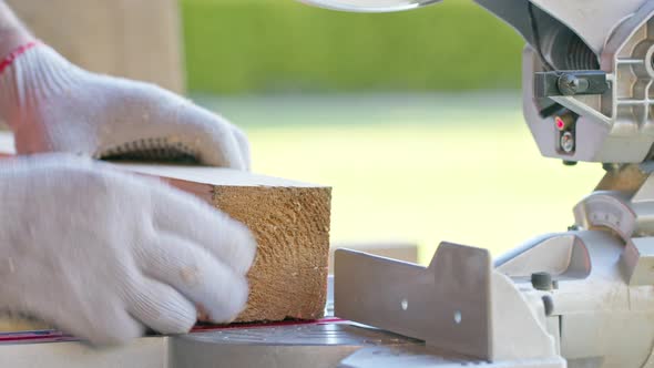 Carpenter Precisely Sets Wooden Workpiece Into the Mitre Saw and Mitres the Bar alt