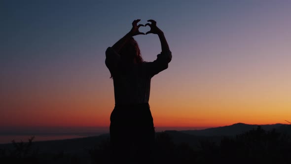 Silhouette Of Girl Making Heart with Hands alt