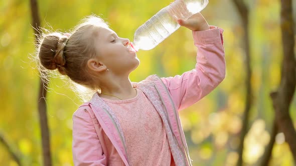 Little girl drinks clean water in the outdoors. Little girl drinks clean water in autumn Park.