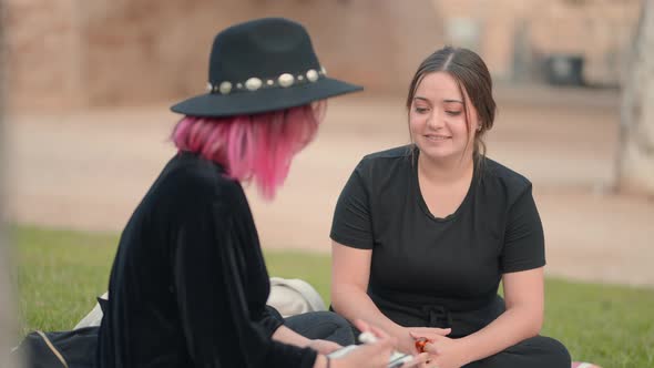Two Caucasian Young Women Chatting While Sitting on the Grass alt