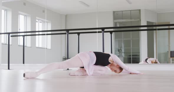 Caucasian female ballet dancer stretching up on the floor and preparing for dance class alt