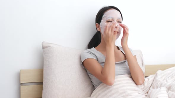 Woman Applying Facial Mask on Face and Sitting on Bed