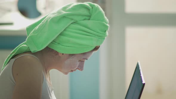 Woman After Bath Sitting at Laptop with a Towel on Head