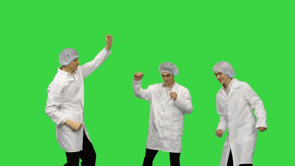 Three Male Doctors in White Robes and Protective Caps Doing Funny Celebration Dance on a Green alt