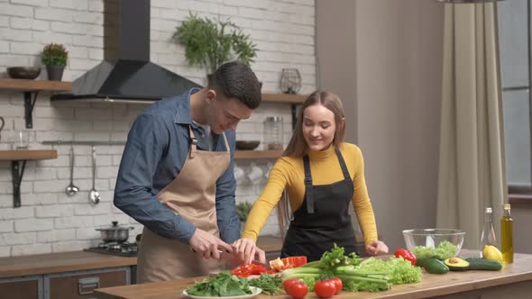 Happy couple enjoying cooking time together at home. Side view of young man cutting vegetables  alt
