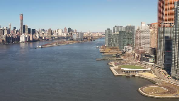 A high angle view looking north over the East River on a sunny day. The drone camera truck right and alt