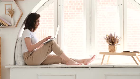 Attractive Woman Working on Laptop Seated at Desk in Cozy Living Room alt