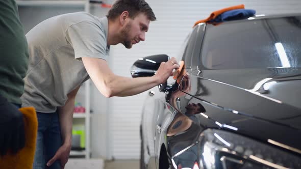 Professional Car Ceramics Worker Applies a Layer of Ceramics Protective Rain Cover on a Car alt