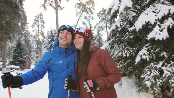 The Happy Couple of Skiers in the Ski Resort of Laughing and Talking Near the Snowcovered Pine Trees