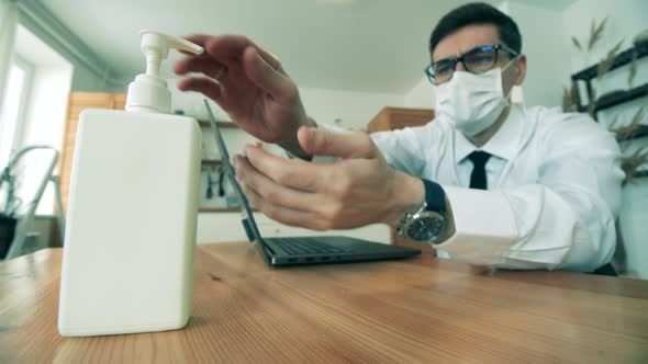 Businessman Is Sanitizing Hands While Working on a Laptop From Home. Man Work at Home in Quarantine alt